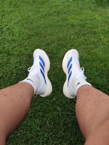 Reviewer's top-down view of their white and blue adidas Adizero EVO SL Running Shoes while sitting on grass.