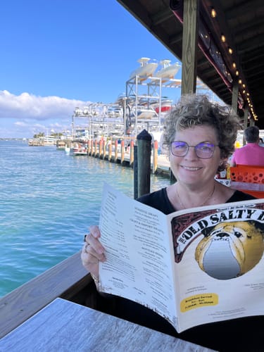 Customer smiling while holding a menu at a table next to the water.