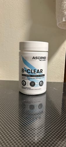 Customer's white bottle of B-CLEAR supplements resting on a dark, textured surface.