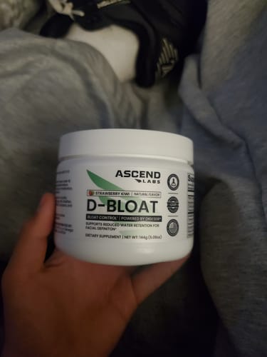 A customer holds up a white tub of D-BLOAT dietary supplement in Strawberry Kiwi flavor.
