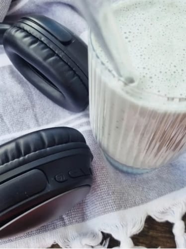 Reviewer's smoothie made with Vanilla Pavlova protein powder in a glass, next to black headphones on a towel.