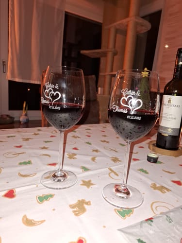 Rezensent zeigt zwei gravierte Leonardo Weingläser, die mit Rotwein gefüllt auf einem festlich gedeckten Tisch stehen.