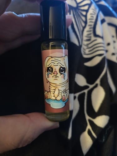 Reviewer holding the Squonk Nugget perfume oil, showing its label with a sad cartoon creature.