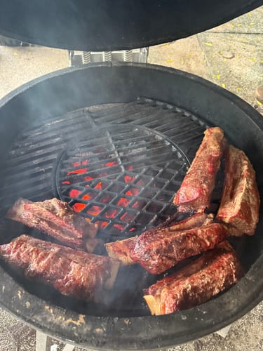 Cliente asando unas Costillas Short Rib en una parrilla redonda de carbón.