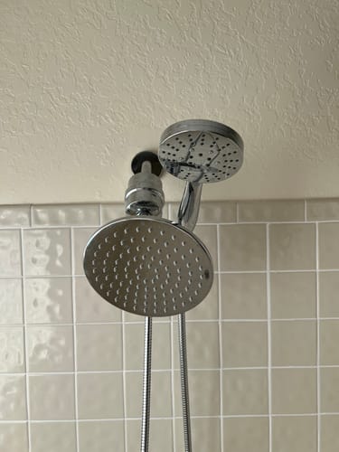 Reviewer's chrome Shower Head Filter installed with a dual shower head set in a tiled shower.