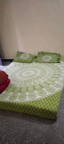 Customer's Flo Mattress Ergo on the floor, made up with a green and white patterned bedsheet and pillows.