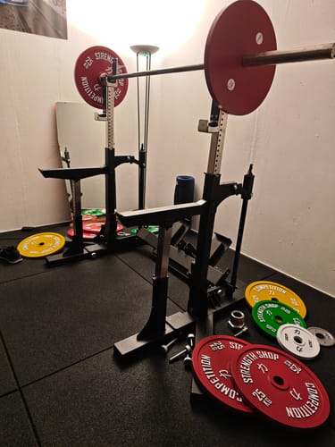 Customer's black Competition Powerlifting Pro Combo Rack set up with a barbell and colorful calibrated plates in a home gym.