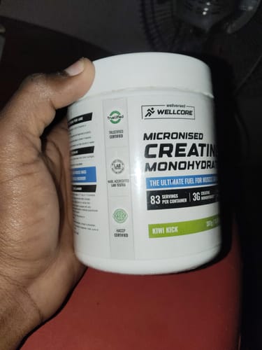 Customer holding a white tub of Wellcore Micronised Creatine Monohydrate, showing the Kiwi Kick flavor label.