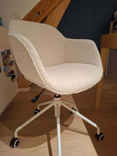 Beoordelaar toont de Nolon Nout-Mare bureaustoel in beige bouclé stof met een witte poot op wieltjes.