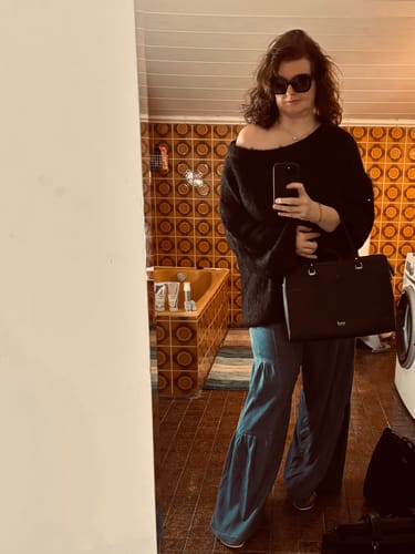 Kundin trägt den ultraweichen, schulterfreien Strickpullover in Schwarz in einem Spiegelselfie.