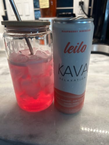 Customer's can of Leilo Kava Raspberry Hibiscus tonic next to a glass filled with the pink drink over ice on a counter.