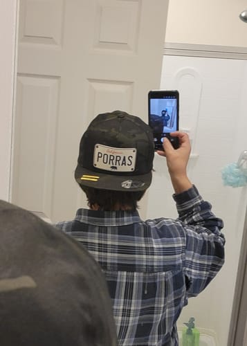 Customer's mirror selfie showing the back of a camo California White Plate Hat with a custom 'PORRAS' patch.