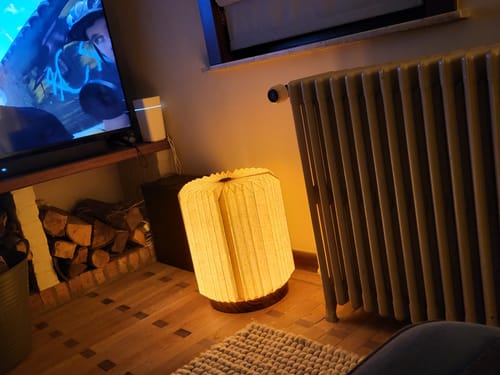 Recensent toont de verlichte by fonQ Linen Tafellamp die op de vloer in een woonkamer staat.