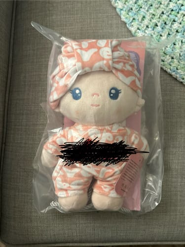 Customer's Personalized Daisy Baby Girl doll inside its clear packaging, wearing a peach and white patterned outfit and headband.