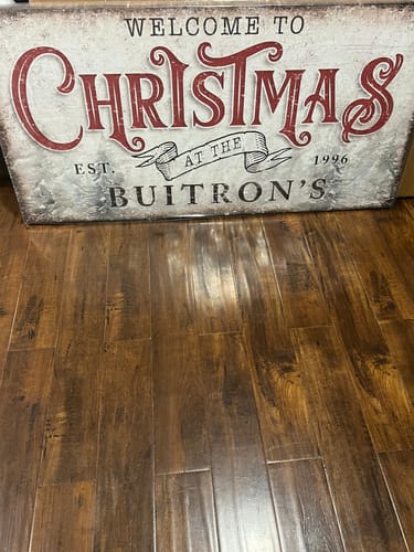 Customer's personalized Family Welcome To Christmas Sign resting on a dark wood floor.