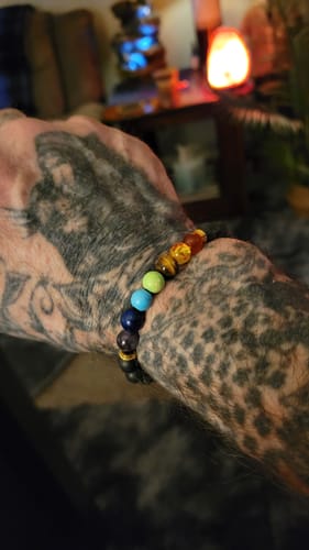 A reviewer's tattooed arm wearing the colorful 7 Chakra Himalayan Stone Bracelet on their wrist.