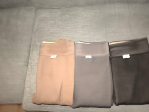 Un client montre trois collants polaires LEGGS pliés, en couleurs beige, gris et noir.