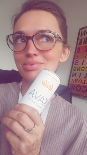 Reviewer thoughtfully holding a can of Leilo Kava Tonic mocktail indoors.