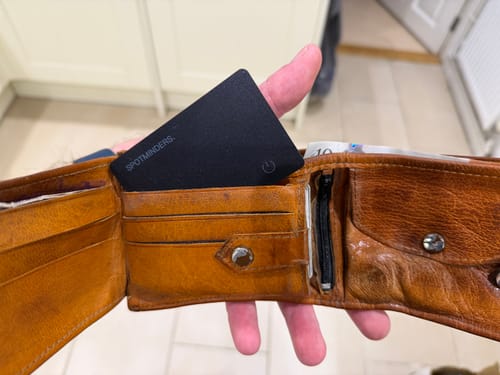 Customer holding a brown leather wallet open, showing the black SPOTMINDERS Tracking Card in a card slot.