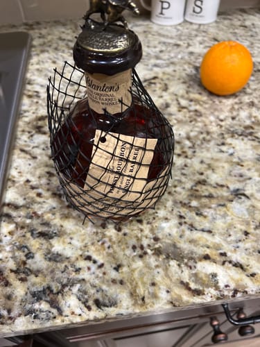 Customer's bottle of Blanton's Bourbon Whiskey in its protective mesh bag, sitting on a granite countertop next to an orange.