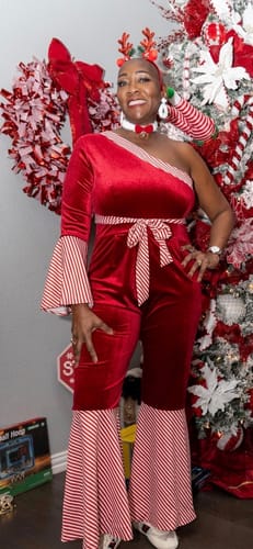 Reviewer smiling in the festive red velvet jumpsuit, showing its one-shoulder design and candy-stripe bell flares.