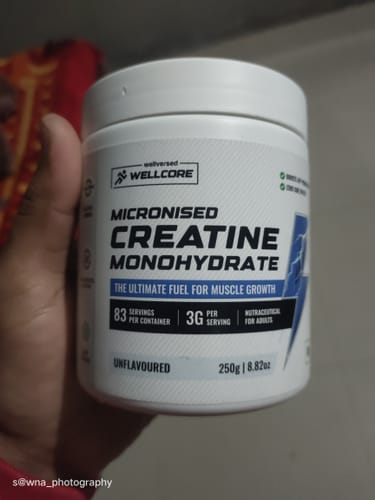 A reviewer's hand holding the white tub of Wellcore Micronised Creatine Monohydrate.