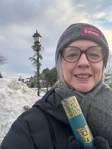 Reviewer smiling outdoors in a snowy setting, holding the Oud Harmony travel size perfume.