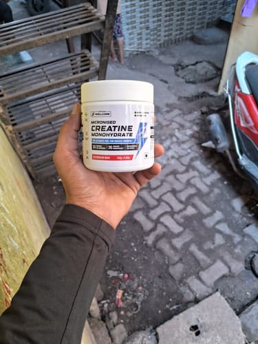 Customer holding a white tub of Wellcore Micronised Creatine Monohydrate supplement outdoors.