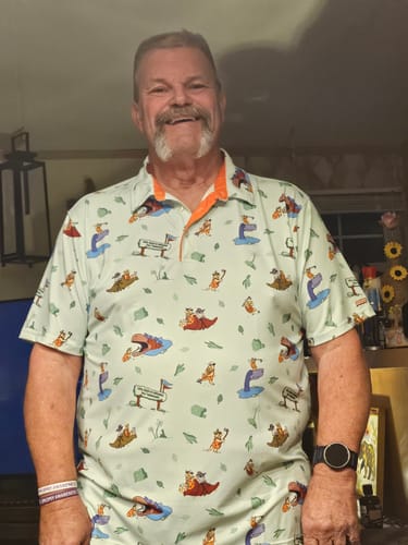 Customer smiles while wearing The Flintstones 'Loyal Order of Dinosaurs' Tourney' polo.