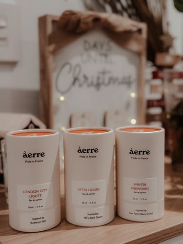 Reviewer's white After Hours perfume bottle, arranged with two other fragrances on a wooden surface.