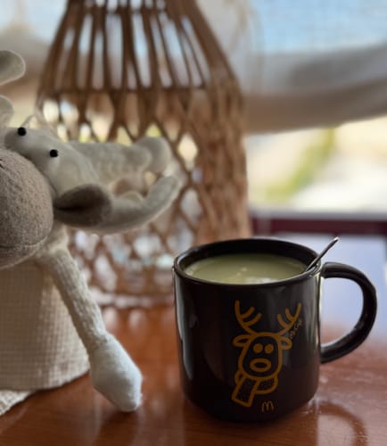 Una clienta muestra su Té Matcha Vainilla Premium preparado en una taza oscura sobre una mesa.