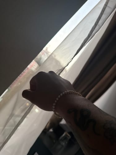Un cliente luce la Pulsera River Pearls en su muñeca tatuada, vista a contraluz cerca de una ventana.