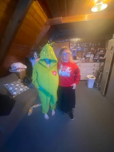 Reviewer wearing the red It Means More Sweatshirt, standing next to a person in a Grinch costume in a room.