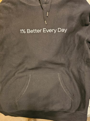 A customer's black Super Heavyweight 1% Better Everyday Hoodie laid flat, showing the white text and kangaroo pocket.