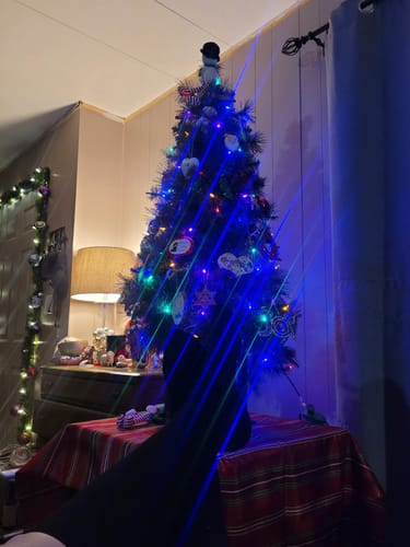 Customer wearing a black compression sock, with their leg resting in front of a decorated Christmas tree.