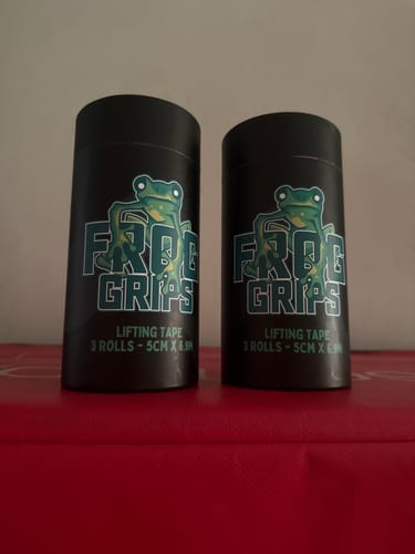 Customer's two black tubes of THUMB TAPE standing side-by-side on a red surface.