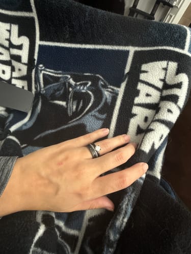 Customer's hand showing The Medusa ring stacked with The Hera and another wedding band against a patterned blanket.