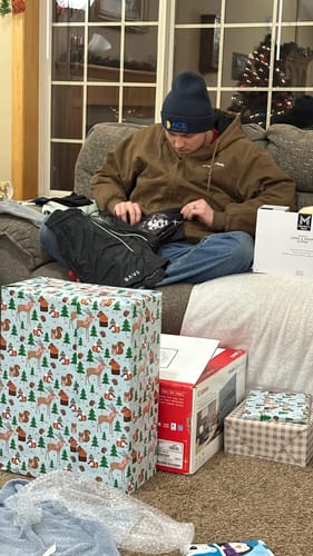 Customer opening a gift of Joshua 1:9 Lion Performance Shorts while sitting on a couch.