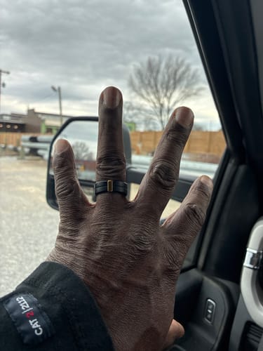 Customer's hand inside a car, wearing the black silicone wedding ring with its stainless steel strip.