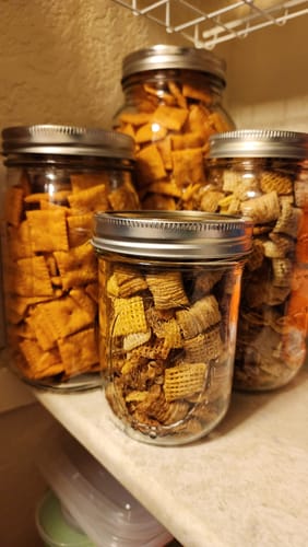 Customer's pantry shelf with four glass jars of snacks, sealed for freshness with the Mason Genie kit.