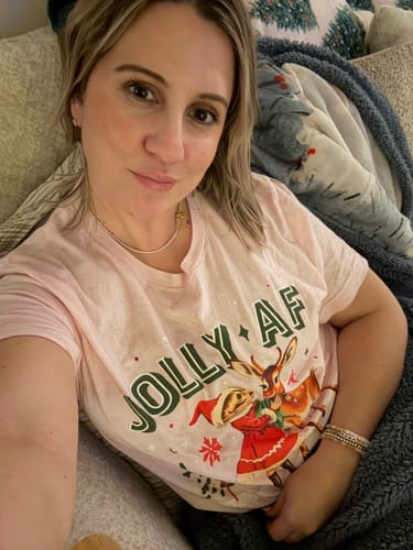 A reviewer takes a selfie while lounging and wearing the pink Jolly AF Tee.