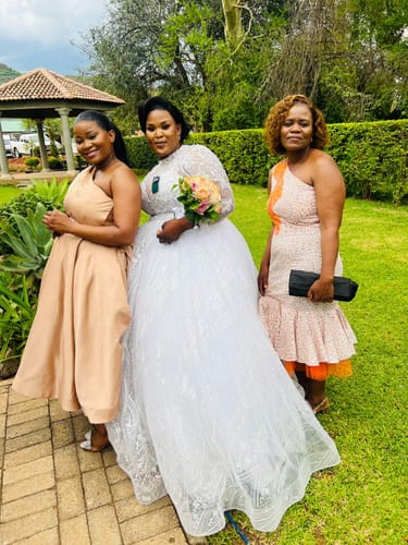 Reviewer wearing the Bahama Blunt Wave wig with a white gown, posing with two other people at an outdoor event.