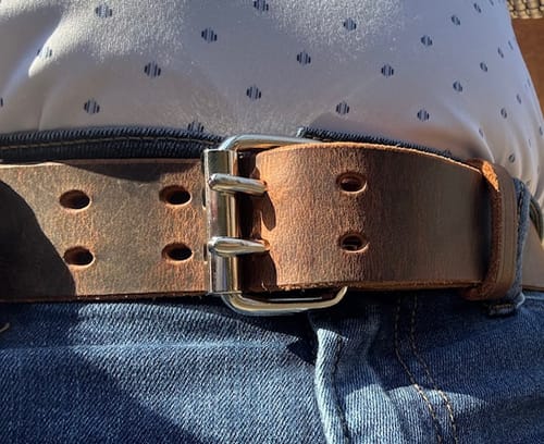 Close-up of a customer wearing the brown leather Legend Double Prong Retro Style belt buckled with blue jeans.