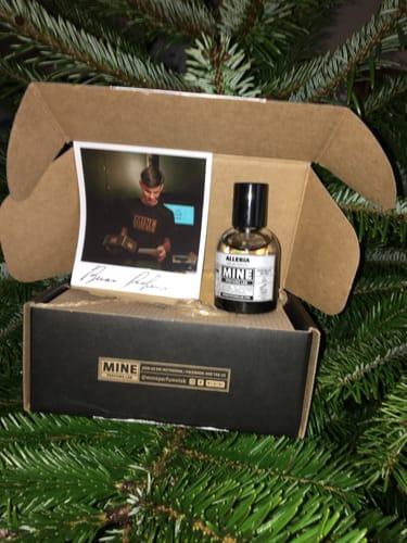 Un cliente mostra il profumo ALLERIA nella sua confezione aperta, posato su rami verdi.