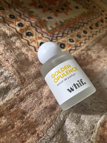 Reviewer's frosted glass bottle of Golden Opulence perfume resting on a patterned rug.
