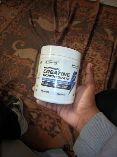 Reviewer holding a white tub of unflavoured Wellcore Micronised Creatine Monohydrate in their hand.