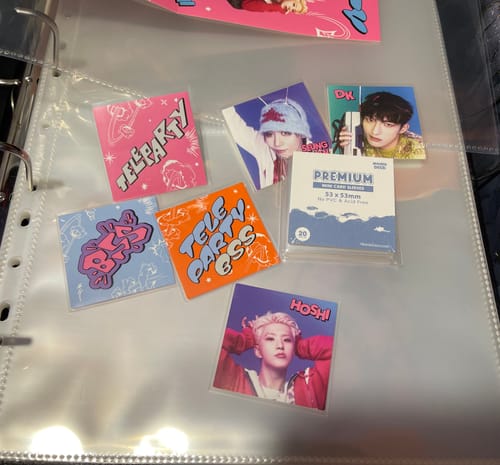 Reviewer's PREMIUM POSTCARD SLEEVES holding K-pop stickers on a binder page, with the product packaging nearby.