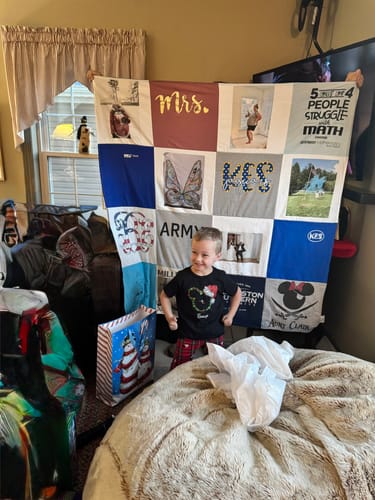 A customer shows a young boy smiling happily in front of his large Premium T Shirt Quilt.