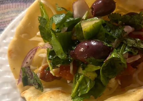 Close-up of a reviewer's taco made with Halal New York Steak, topped with fresh greens and olives.