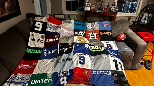 Customer's finished Premium T-Shirt Quilt, made from various sports jerseys, displayed on a couch.